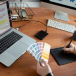 Designer reviewing font licensing options on computer screen with client documents and typography samples visible on desk