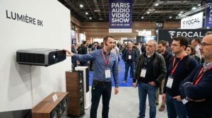 An engineer presenting a new home cinema projector and surround sound system to visitors at the Paris Audio Video Show 2026 exhibition floor