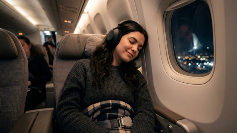 Passenger wearing noise canceling headphones in an airplane window seat.
