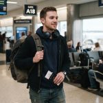 Man wearing black lightweight JBL headphones around neck at airport terminal.
